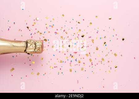 Bottiglia di champagne dorato con confetti su sfondo rosa. Concetto minimo di festa. Foto Stock