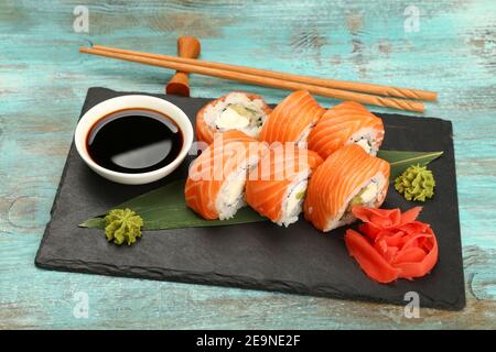 Set da primo piano di sei panini di sushi Filadelfia con salmone crudo servito sulla tavola di ardesia nera su un tavolo blu, vista ad angolo alto Foto Stock