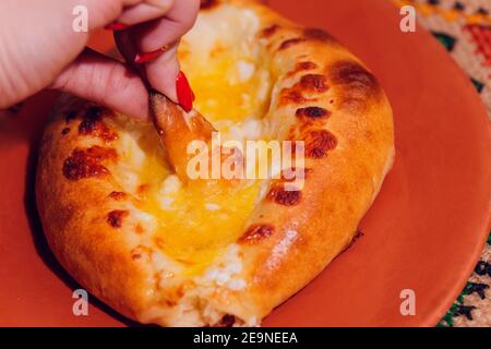 La donna sta mangiando il khachapuri adjariano con le mani, schiacciando il tuorlo d'uovo Foto Stock
