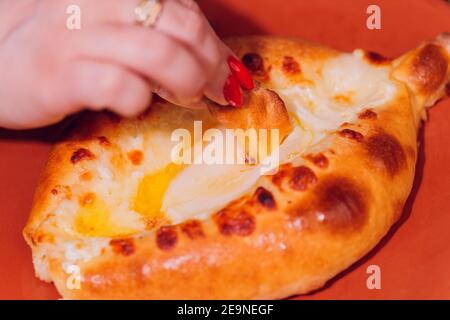 La donna sta mangiando il khachapuri adjariano con le mani, schiacciando il tuorlo d'uovo Foto Stock