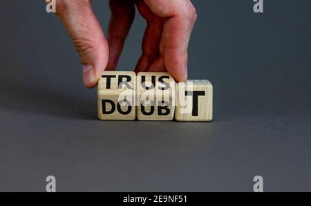 Simbolo di fiducia o dubbio. L'uomo d'affari capovolge i cubi di legno e cambia il dubbio di parola alla fiducia. Splendido sfondo grigio, spazio per la copia. Affari e fiducia o Foto Stock