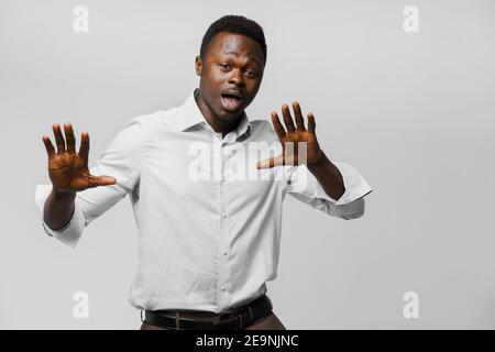 L'uomo d'affari nero africano balla e apre la bocca. Uomo dalla pelle scura con camicia bianca su sfondo bianco. Annuncio per la consegna online Foto Stock