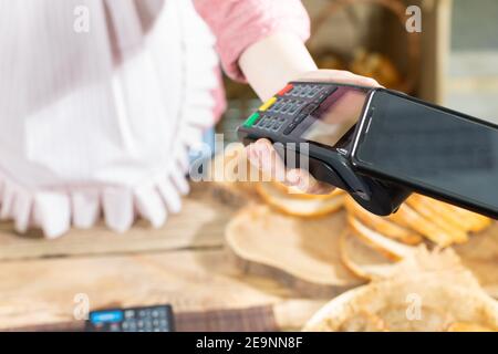 Il cliente paga il pane acquistato tramite il terminale di pagamento utilizzando un telefono cellulare. Pagamento senza contanti. Azienda panificio negozio. Foto Stock