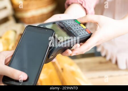 Il cliente paga il pane acquistato tramite il terminale di pagamento utilizzando un telefono cellulare. Pagamento senza contanti. Azienda panificio negozio. Foto Stock