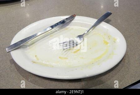 Piatto vuoto sporco con coltello e forchetta dopo colazione pasto di uova in un ristorante. Foto Stock