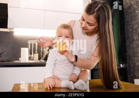 Giovane madre caucasica dà il bambino a bere da bottiglia di plastica. Foto Stock