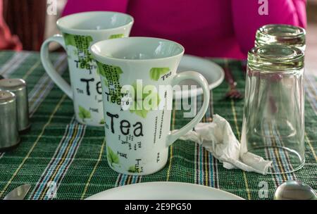 Badami, Karnataka, India - 7 novembre 2013: Primo piano di set di tazze da tè bianche con impresso artistico sul tavolo con panno verde e bicchieri. Foto Stock