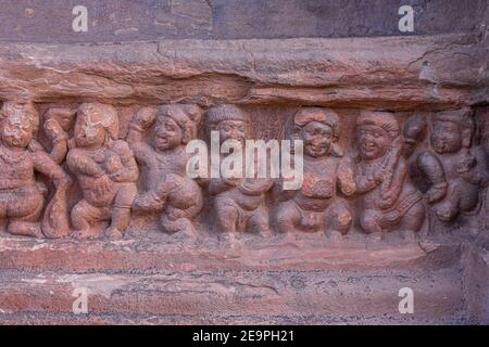 Badami, Karnataka, India - 7 novembre 2013: Templi in grotta sopra il lago Agasthya. Primo piano di restone scultura di fila di piccole figure umane danzanti e. Foto Stock