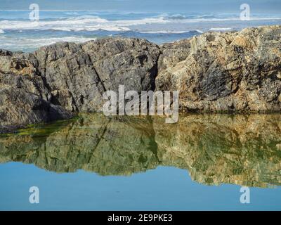 Bellissimi riflessi. Le rocce che costeggiano la piscina di roccia si riflettevano e si specchiavano nell'acqua salata, guardando verso l'Oceano Pacifico oltre. Chiarezza Foto Stock