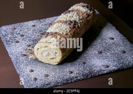 Vista prospettica di un braccio gitano fatto a mano di cioccolato e. crema con scaglie di cioccolato bianco e scuro su piastra di ardesia Foto Stock