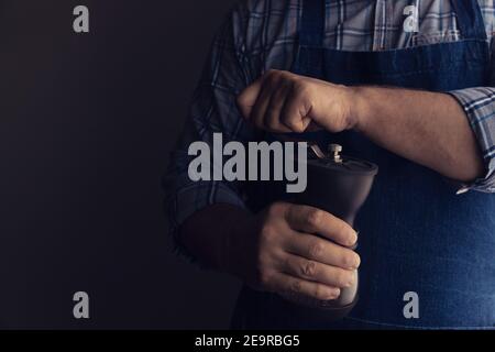 Il barista macina i chicchi di caffè in un macinacaffè manuale. Sfondo scuro. Tasto basso Foto Stock