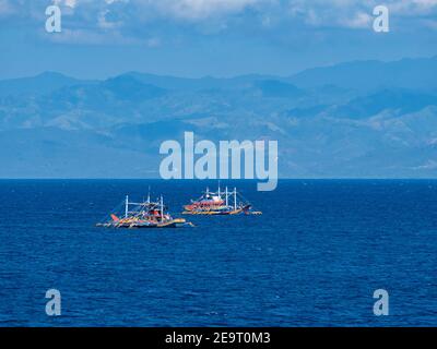 Due tradizionali tonniere in legno con outrigger nella baia di Sarangani, con le montagne di Bayan ng Glan, Sarangani e Davao del sur nella b Foto Stock