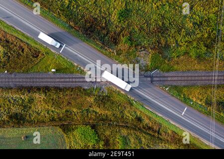 vista aerea di binari ferroviari che attraversano una strada asfaltata con auto in zona rurale Foto Stock