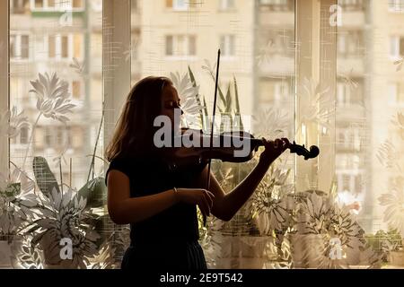 Silhouette di una giovane ragazza, un musicista. Suonare il violino sullo sfondo della finestra. Foto Stock