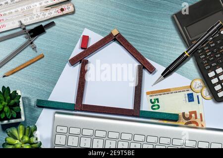 Piccola casa in legno fatta di blocchi giocattolo sulla scrivania, con valuta Euro, calcolatrice, righello pieghevole. Concetto di investimenti immobiliari. Foto Stock