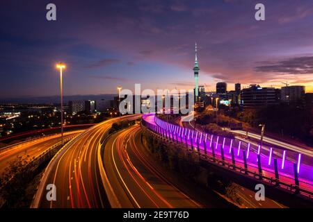 Vista dello skyline di Auckland, della Sky Tower e dell'autostrada con percorsi in auto all'alba. Foto Stock