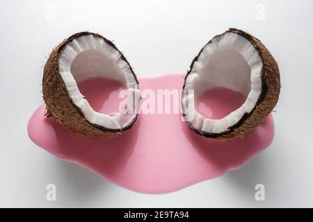 Layout creativo fatto di cocco a metà con versamento di latte rosa. Concetto di cibo minimo. Foto Stock