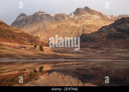 Bella alba invernale su Blea Tarn nel Lake District con Pikes Langdale innevate in lontananza Foto Stock