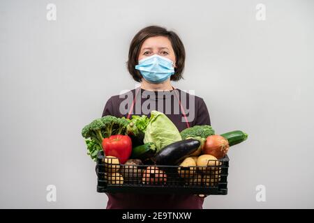 Donna che indossa una maschera e che tiene il cesto pieno di prodotti cercando di fare una vendita. Consegna durante la pandemia di Covid. Foto Stock