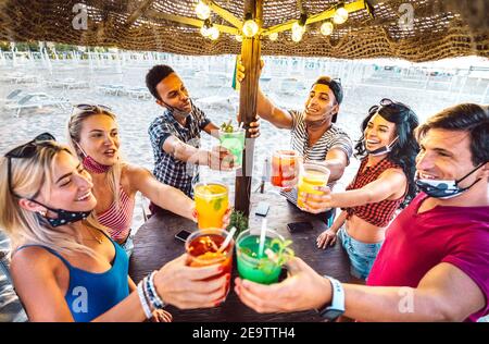 Giovani amici alla moda che tostano al cocktail bar sulla spiaggia chiringuito con Maschera facciale - nuovo concetto estivo normale con la gente che ha divertimento insieme Foto Stock