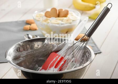 Recipiente in metallo, frusta e spatola in silicone. Un dessert con panna montata Foto Stock