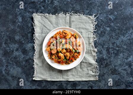 Creola jambalaya con salsicce affumicate, carne di pollo e verdure su piatto su sfondo di pietra blu con spazio libero. Vista dall'alto, disposizione piatta, primo piano Foto Stock