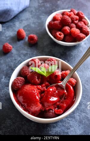 Sorbetto al lampone, paletta per gelato con frutti di bosco freschi in una ciotola su sfondo di pietra blu. Gustoso dessert estivo freddo. Vista ravvicinata Foto Stock