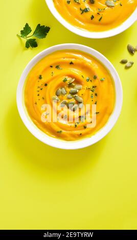 Purea di zucca con semi in ciotola su sfondo giallo con spazio di testo libero. Concetto di alimentazione sana. Vista dall'alto, disposizione piatta Foto Stock