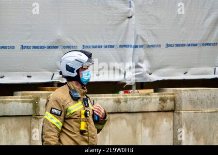 Un comandante dei vigili del fuoco della Brigata dei vigili del fuoco di Londra, indossando una maschera facciale, usando una radio per comunicare con i colleghi sulla scena di un incidente importante.UK Foto Stock