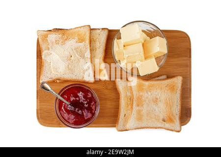 Tavolo per la colazione del mattino con pane tostato fresco su un banco di taglio in legno, marmellata di fragole e burro. Isolato su sfondo bianco. Vista dall'alto, spazio di copia Foto Stock