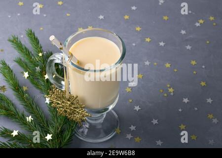 Eggnog fatto in casa con timo e arancio in un bicchiere su sfondo grigio con un ramo di un albero di Natale e decorazioni natalizie, focu selettivo Foto Stock