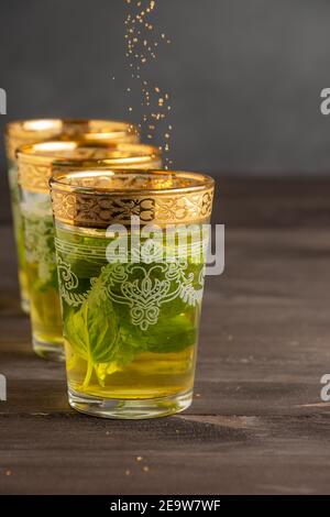 Primo piano di bicchieri da tè alla menta decorati, con caduta di zucchero di canna, fuoco selettivo, su tavolo di legno scuro, sfondo scuro, verticale Foto Stock