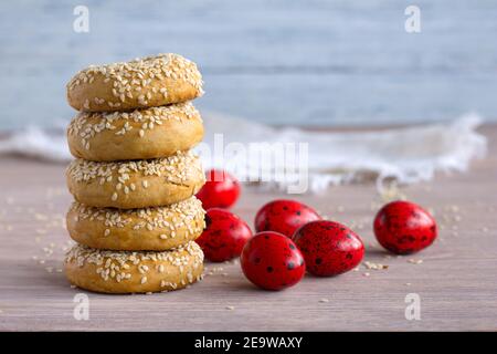 Biscotti tradizionali greci di Pasqua con semi di sesamo e uova colorate sul tavolo di legno, fuoco selettivo, spazio libero Foto Stock