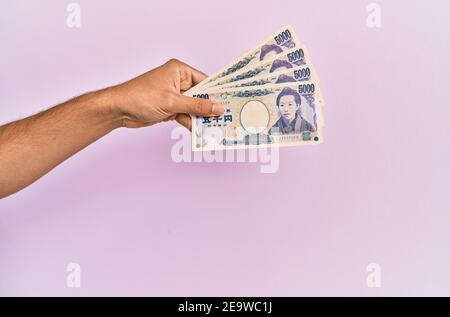 Mano ispanica che tiene 5000 yen giapponesi su sfondo rosa isolato. Foto Stock