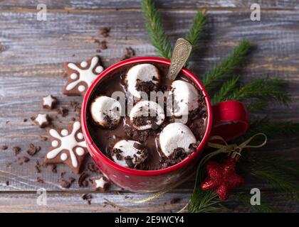 Cioccolata calda con marshmallows e cioccolato grattugiato in una tazza rossa con biscotti e albero di natale su un tavolo di legno, stile rustico. delizioso natale Foto Stock