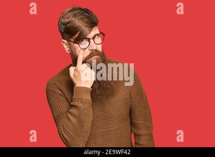 Giovane irlandese rosso uomo che indossa abiti casual e bicchieri che punta all'occhio che ti guarda gesto, espressione sospetta Foto Stock