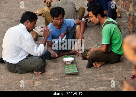 BAGAN, MYANMAR - 18 NOVEMBRE 2015: Uomini poveri che giocano a giocare sulla strada, vista laterale del gruppo di poveri uomini a piedi nudi seduti sul marciapiede giocando gioco orientale Foto Stock