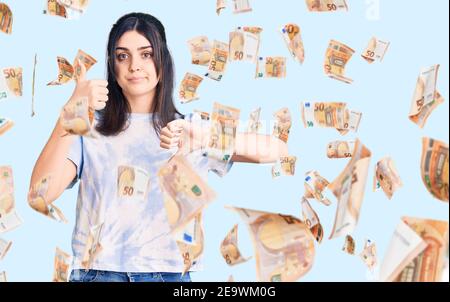 Giovane bella ragazza che indossa una t-shirt casual facendo i pollici su e giù, discordia e l'espressione di accordo. Conflitto pazzo Foto Stock