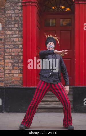 York, Inghilterra - Febbraio 24 2018: Un giocatore di strada di juggler di contatto che usa una palla di vetro in un vestito rosso nero coordinato si esibisce nel centro della città Foto Stock