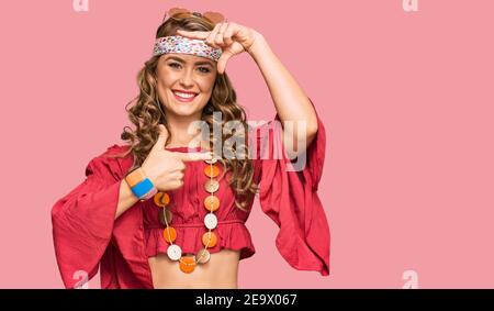 Giovane bionda ragazza in stile bohémien e hippie sorridente rendendo cornice con mani e dita con volto felice. Creatività e concetto di fotografia. Foto Stock