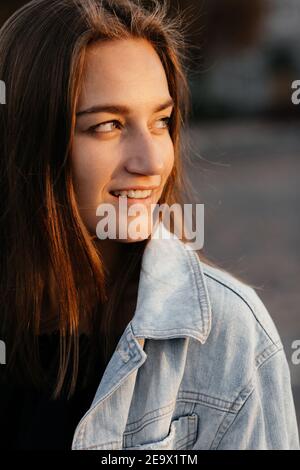 Affascinante ragazza in jeans giacca guardando al lato e sorridente. Ritratto di ragazza Foto Stock