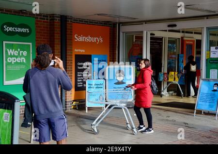 Uomo che mette sulla maschera fuori Sainsbury's haringey london con maschera cartelli e acquirenti Foto Stock