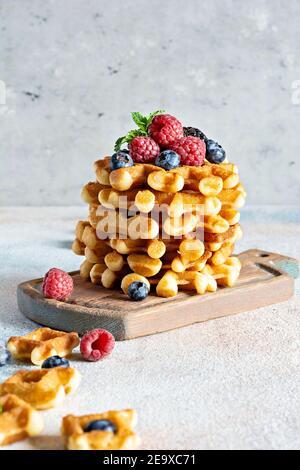 Waffle belgi freschi e croccanti per colazione con frutti di bosco maturi (lamponi, mirtilli, more), menta e zucchero in polvere su una tavola di legno su un Foto Stock