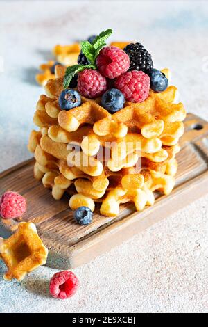 Waffle belgi freschi e croccanti per colazione con frutti di bosco maturi (lamponi, mirtilli, more), menta e zucchero in polvere su una tavola di legno su un Foto Stock