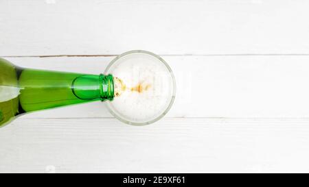 Versare la birra dalla bottiglia in un bicchiere su un tavolo di legno bianco. Vista dall'alto. CopySpace. Foto Stock