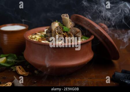 Gosht o Agnello Biryani preparato in riso Basmati servito con yogurt in ciotola di terracotta. Messa a fuoco selettiva Foto Stock