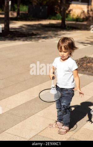 il bambino giocoso in una t-shirt bianca gioca il bambinton in parcheggia in una giornata estiva di sole Foto Stock