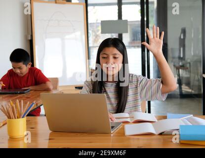 asian ragazza studentessa alzando la mano studiando la lezione di apprendimento on-line. riunione a distanza formazione a distanza a casa Foto Stock