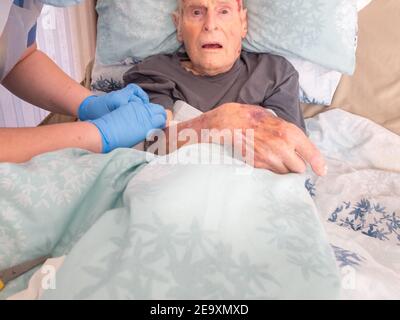 Il novantacinque anni ha il braccio ferito bendato A casa sua da un nurse.He distretto in visita non è in grado lasciare il letto o la casa a causa della fragilità Foto Stock