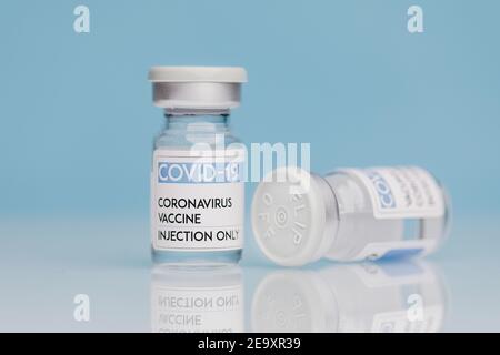 Fiale di vetro con vaccino COVID 19 poste sul tavolo su sfondo blu Foto Stock